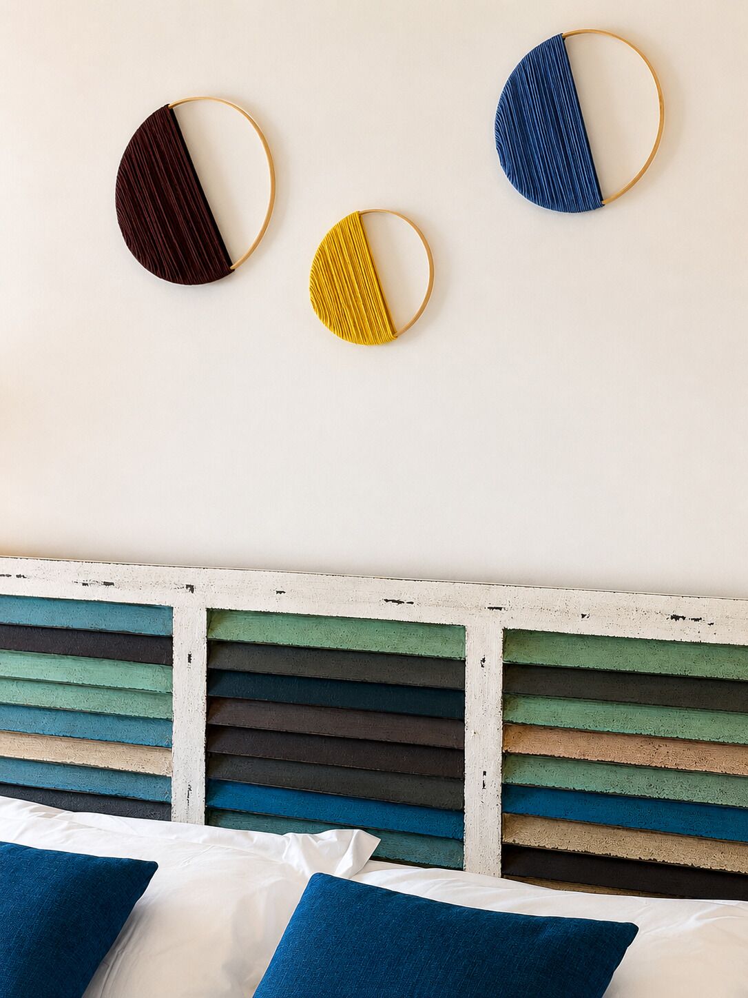 A bed with white and blue bedding, a multicolored headboard, and three wall-mounted circular mirrors.