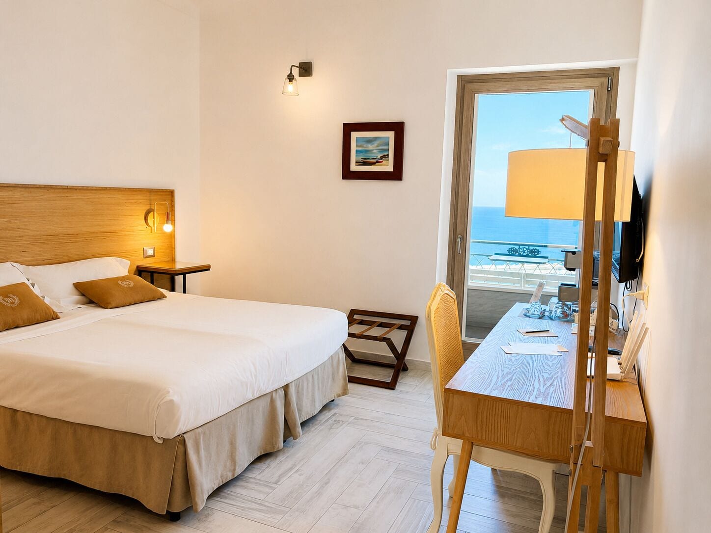 Une chambre d’hôtel comprenant un lit, une table de chevet, une lampe, une chaise, un bureau et une vue sur la mer, visible par la porte.