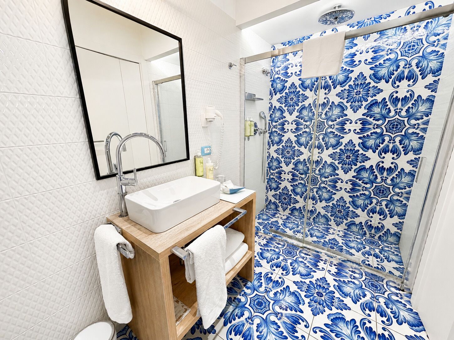 A bathroom with a white sink, mirror, and shower with blue floral tiles.