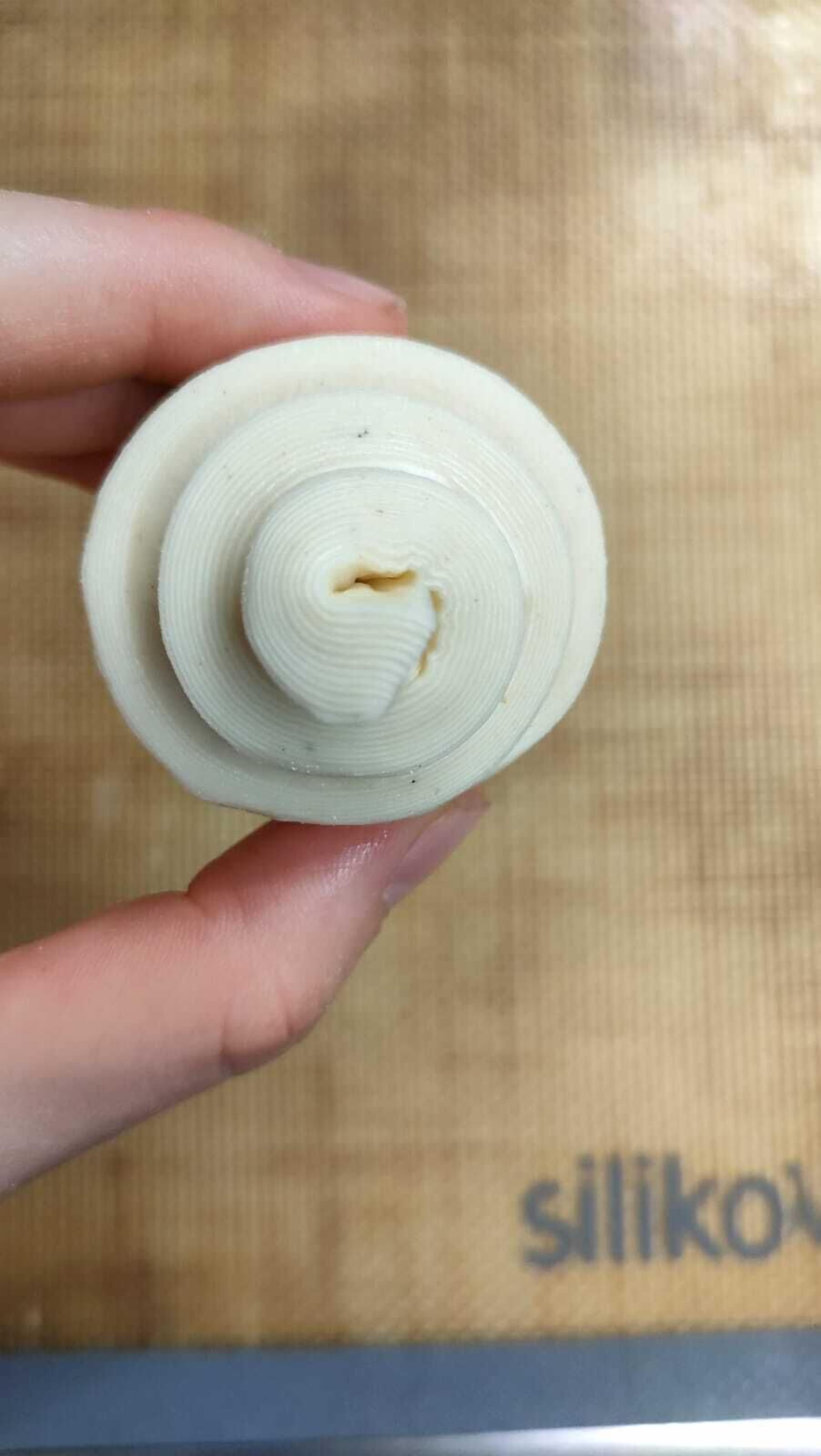Una mano sostiene un objeto cilíndrico con un diseño en espiral, posiblemente un recipiente o una herramienta, sobre un fondo que muestra parcialmente la palabra 'siliko'.