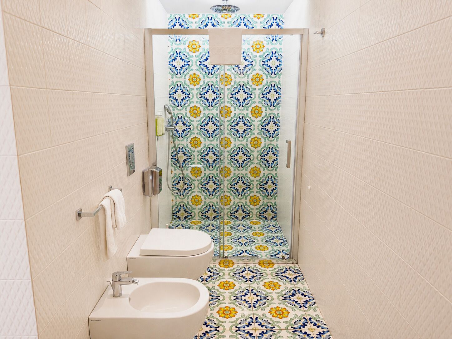 Une salle de bain équipée d’une douche, de toilettes et d’un bidet, avec des carreaux décoratifs et un porte-serviettes.