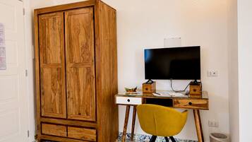 Ein Zimmer mit einem Holzschrank, einem Schreibtisch mit Fernseher, einem gelben Stuhl und fußbodenhohen, gemusterten Fliesen.