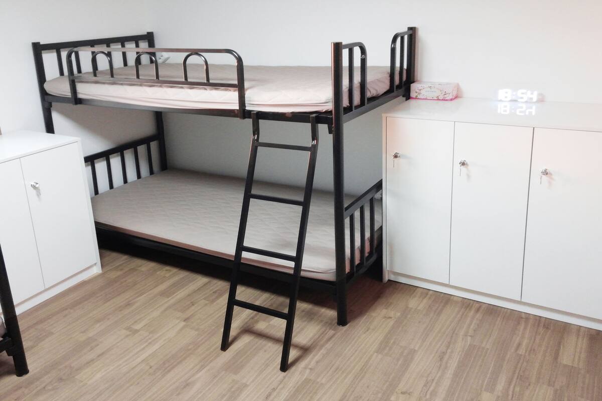 Una cama litera con escalera, un armario blanco y un mueble pequeño.