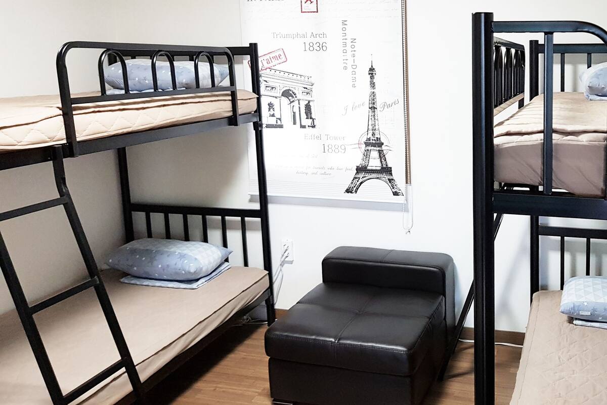 Un dormitorio con literas, un pequeño taburete negro y un cartel del Torre Eiffel.