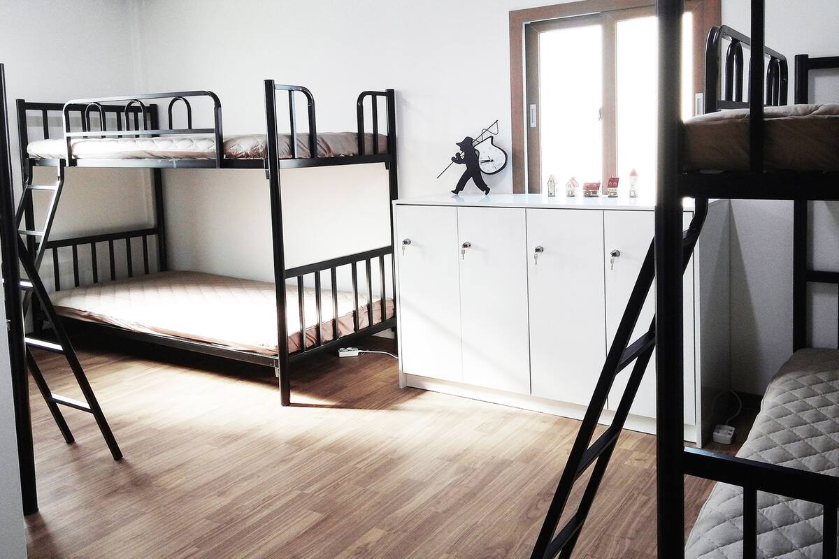 Habitación con literas, un armario blanco y un ventanal pequeño.