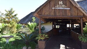 Un'area di accoglienza con tetto di paglia e struttura in legno, circondata da piante tropicali.