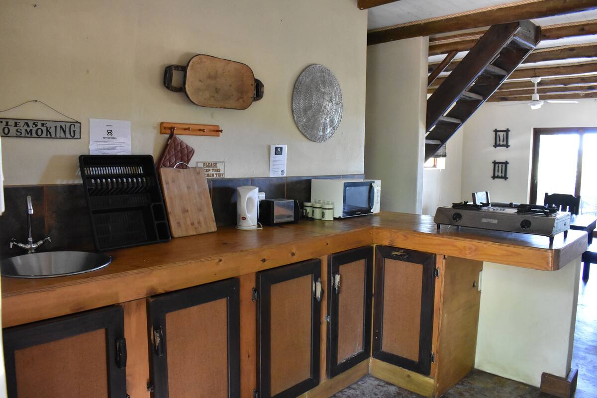 A kitchen with wooden cabinets, a sink, a stove, and a microwave. There are signs on the wall, including one that says "Please Keep This Clean."