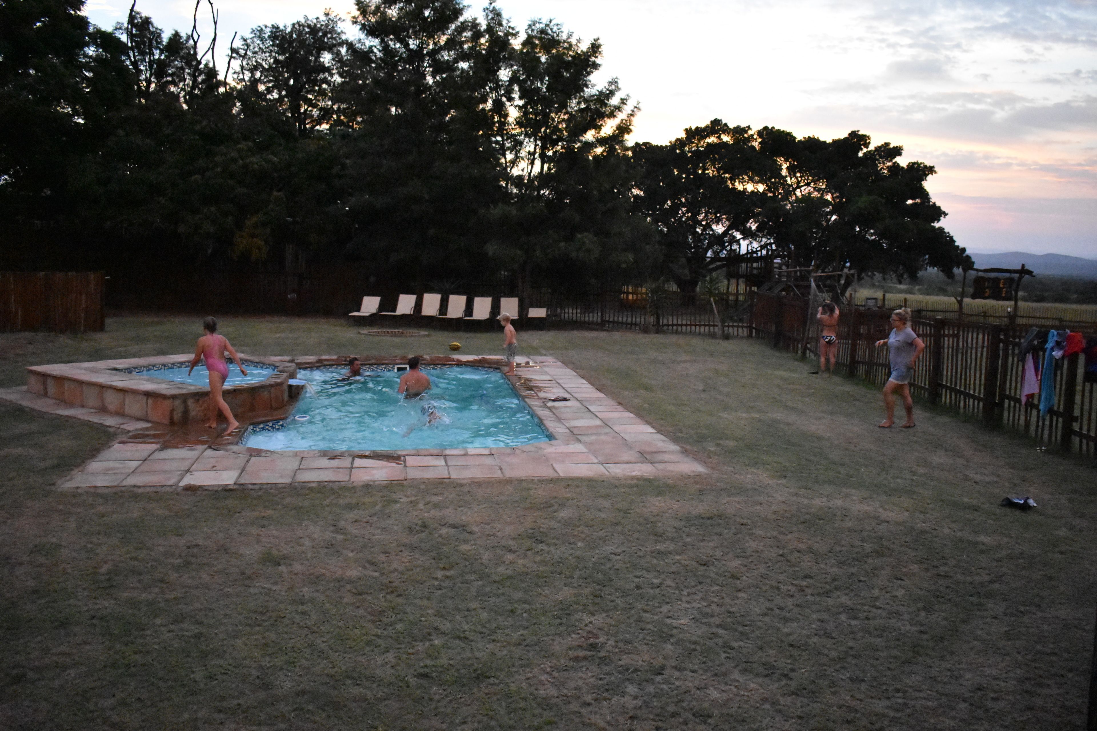 Un jardin avec une piscine, une terrasse en bois et une zone délimitée par une clôture.