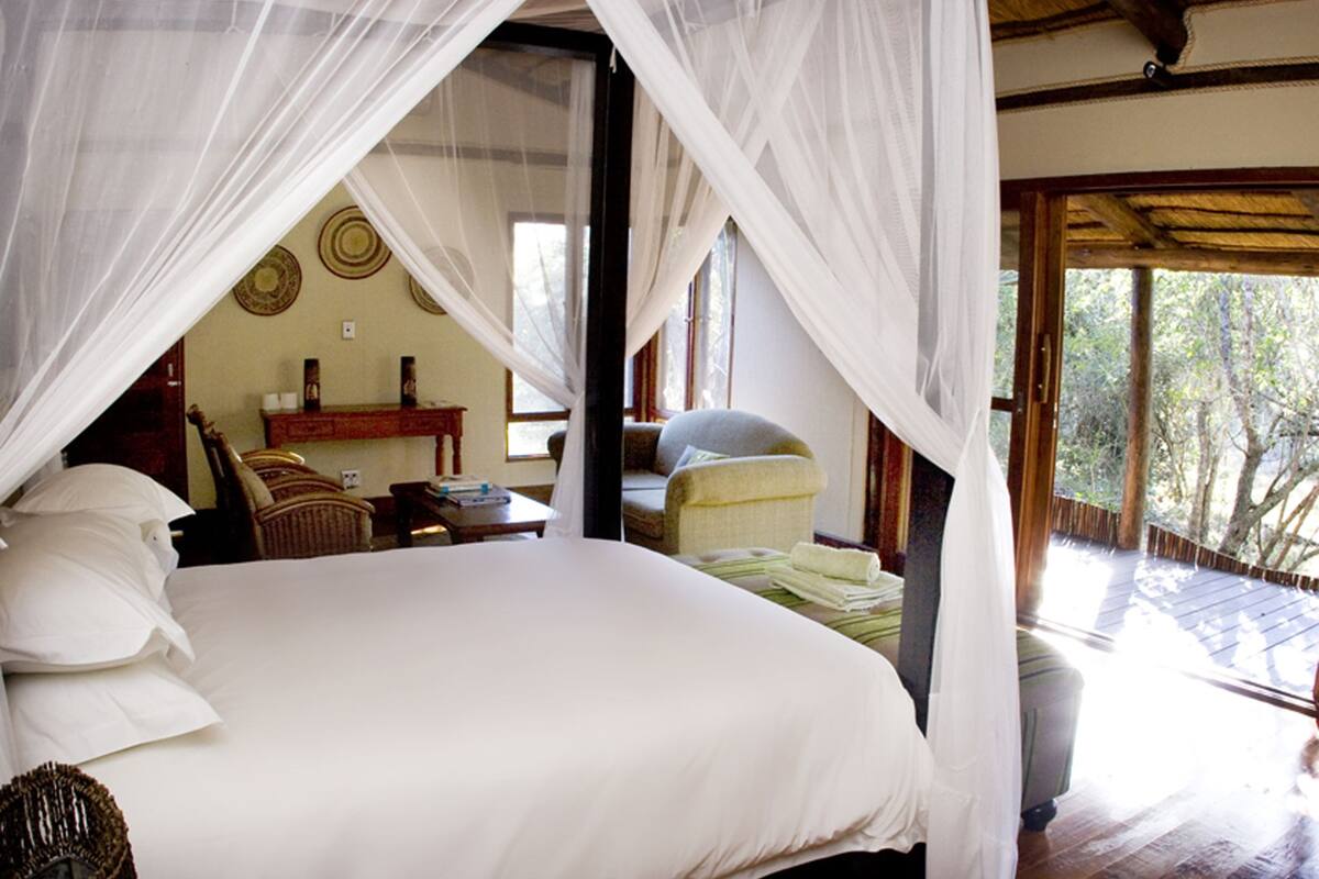 A bedroom with a large bed, a chair, a small table, and a window with a view of trees.