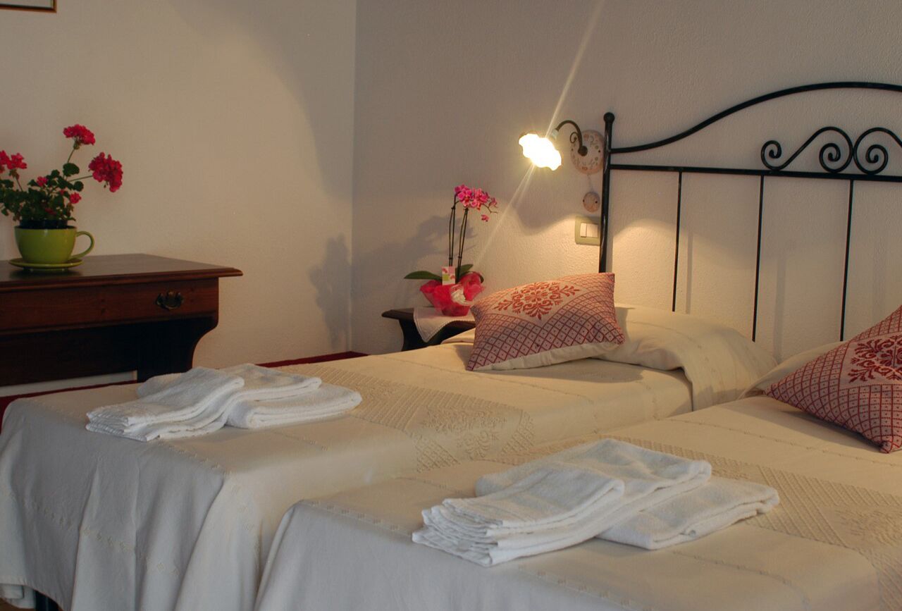 Ein Hotelzimmer mit zwei Betten, jeweils ausgestattet mit ordentlich gefalteten weißen Handtüchern, einem Nachttisch mit einer grünen Tasse und rosa Blumen sowie einer Wandleuchte.