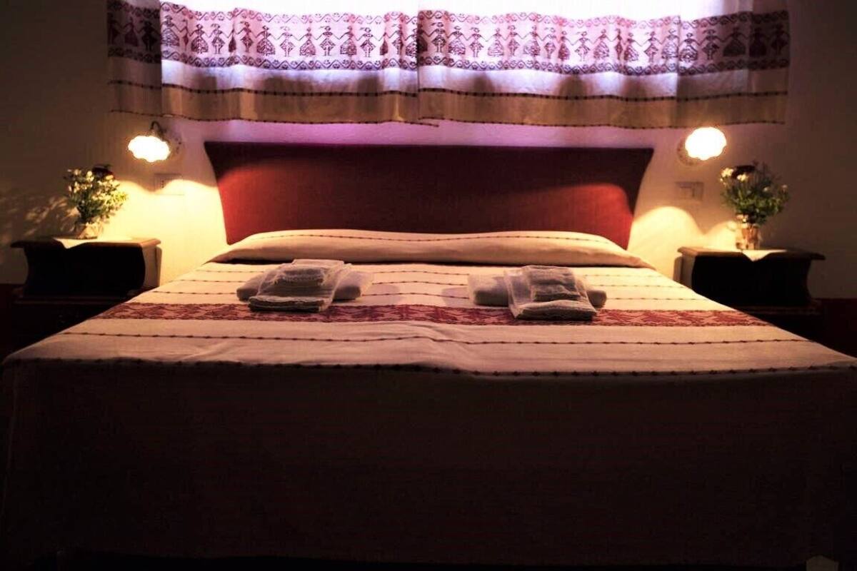 A neatly made bed with a red headboard, two bedside tables with lamps, and a patterned curtain above.