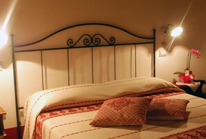 A bed with a headboard, pillows, and a bedside table with a lamp and a vase of flowers. - Country House S'Ozzastru (Dorgali)