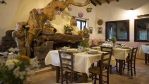 A rustic dining area with wooden tables and chairs, a stone fireplace, and decorative flowers. - Country House S'Ozzastru (Dorgali)