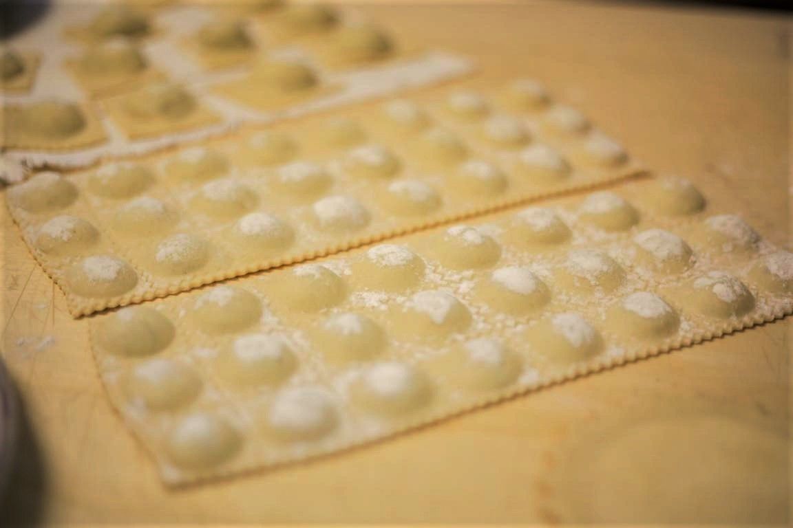 A close-up of a baking sheet with multiple rows of uncooked pasta dough balls.