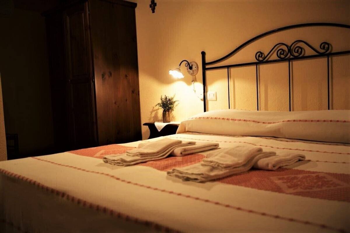 A neatly made bed with folded towels, a bedside lamp, and a wooden wardrobe in a hotel room.