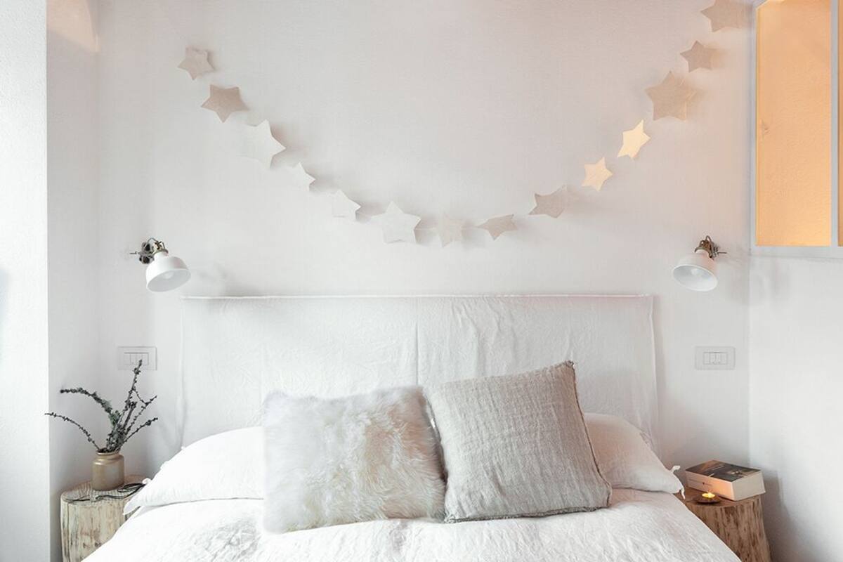A bedroom with a white bed, two pillows, a nightstand with a lamp, and a wall with star decorations.