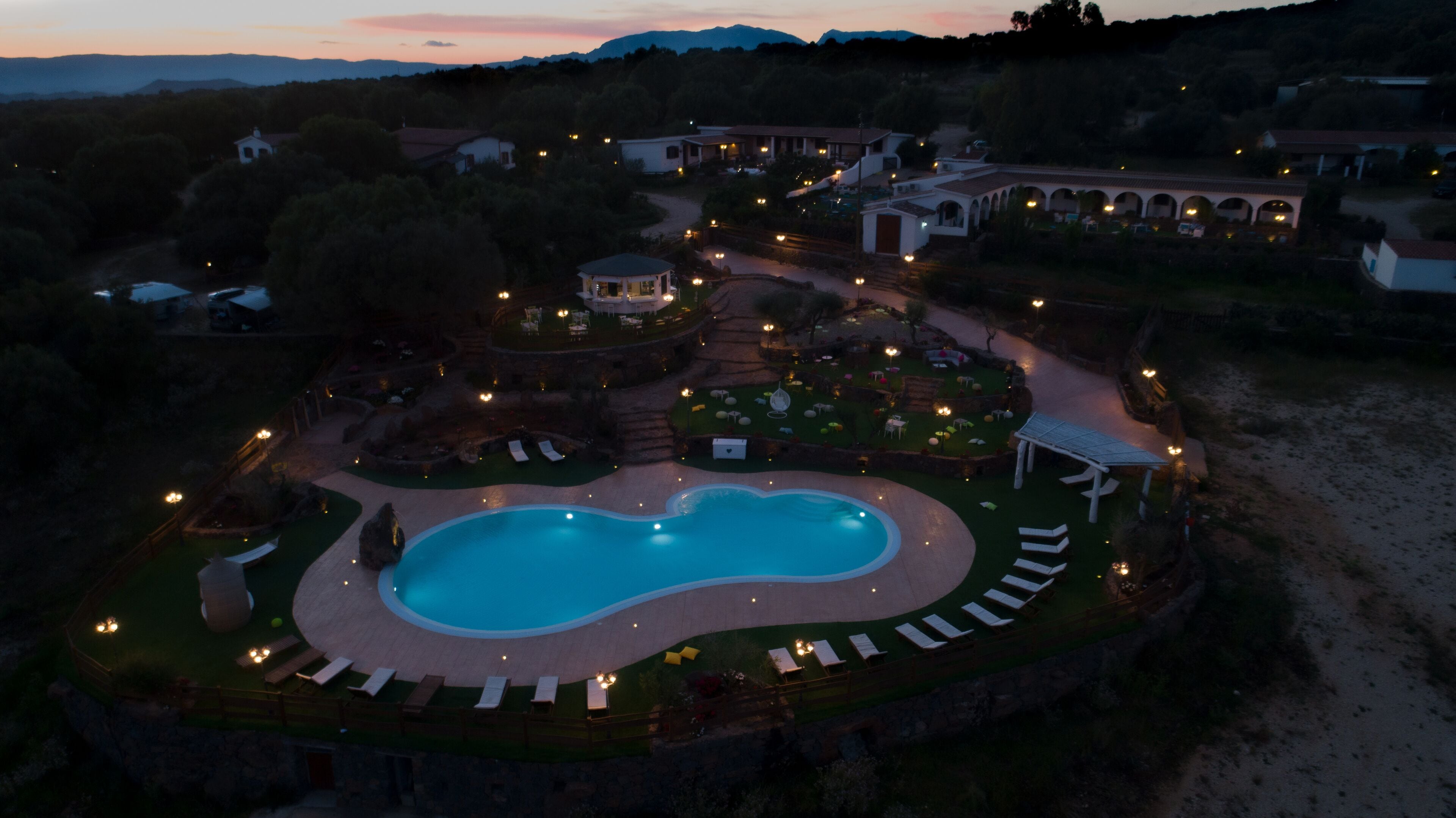 An aerial view of a resort with a large swimming pool, lounge areas, and a well-lit courtyard.