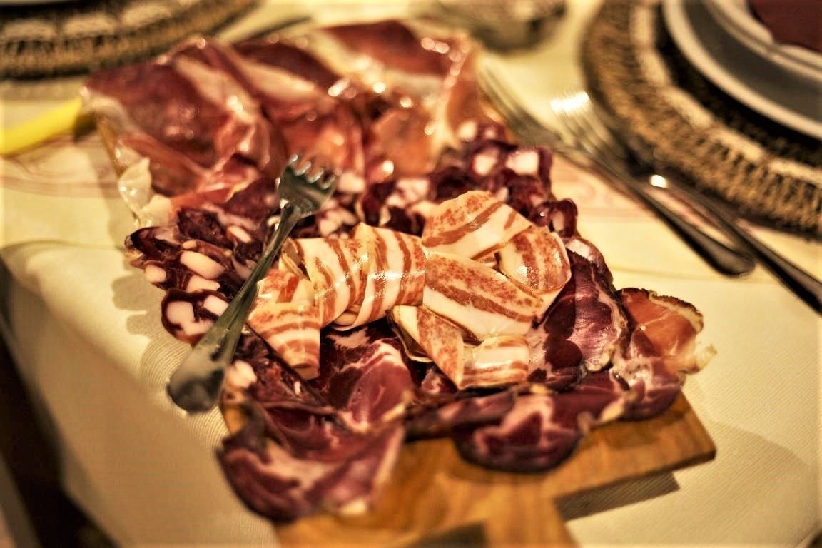 A wooden board with various meats, including bacon and possibly ham, on a table.