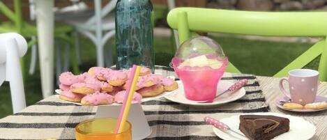 Mesa al aire libre con mantel a cuadros, diferentes platillos, un vaso de té helado y un jarrón con flores.