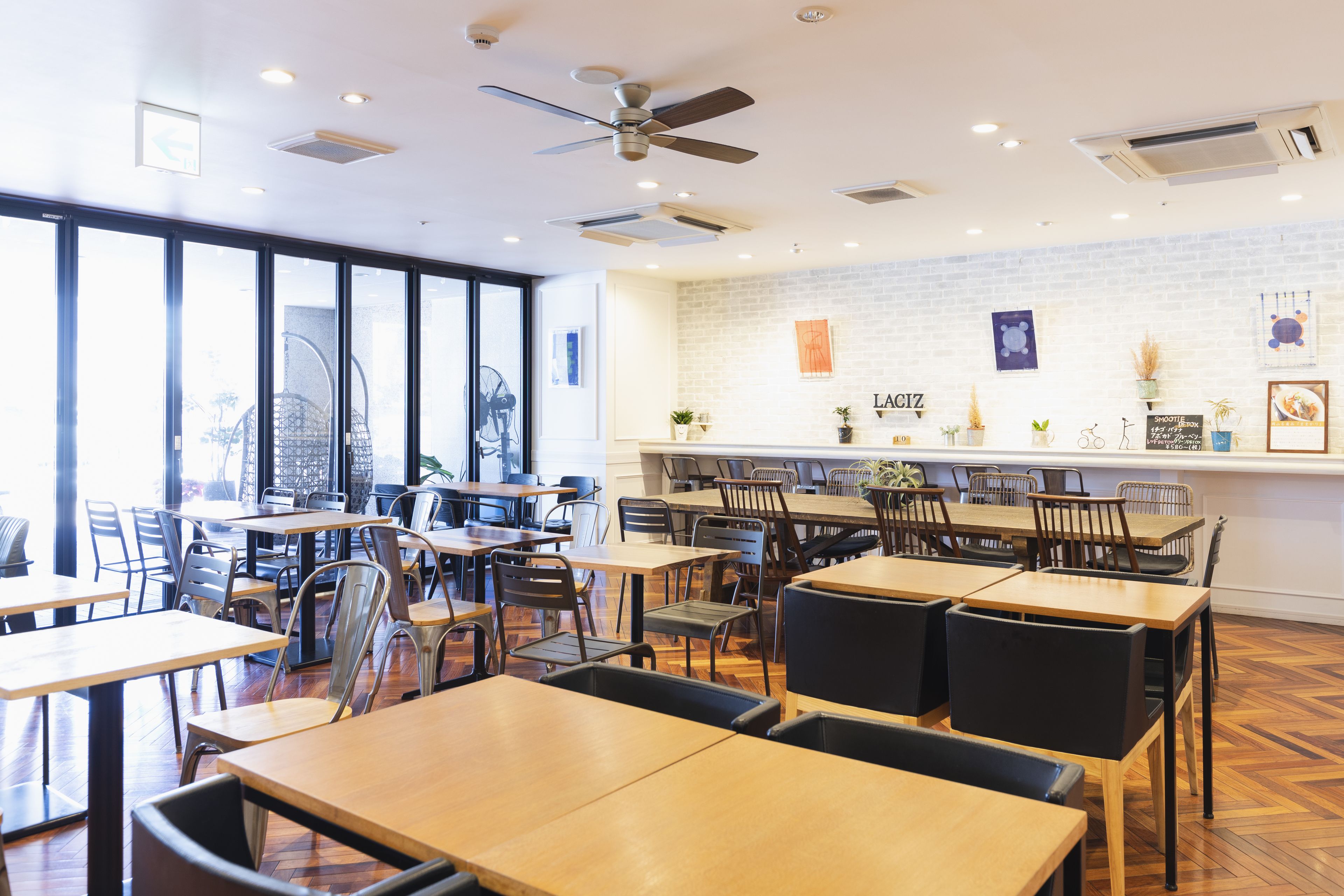 Un restaurante con varias mesas y sillas, un muro de ladrillo con obras de arte y un ventilador de techo.