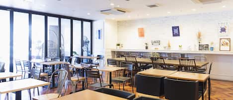 Un restaurante con varias mesas y sillas, un muro de ladrillo con obras de arte y un ventilador de techo.