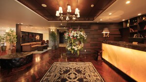Un vestíbulo de hotel con una recepción, una araña, un sofá y un arreglo floral decorativo.