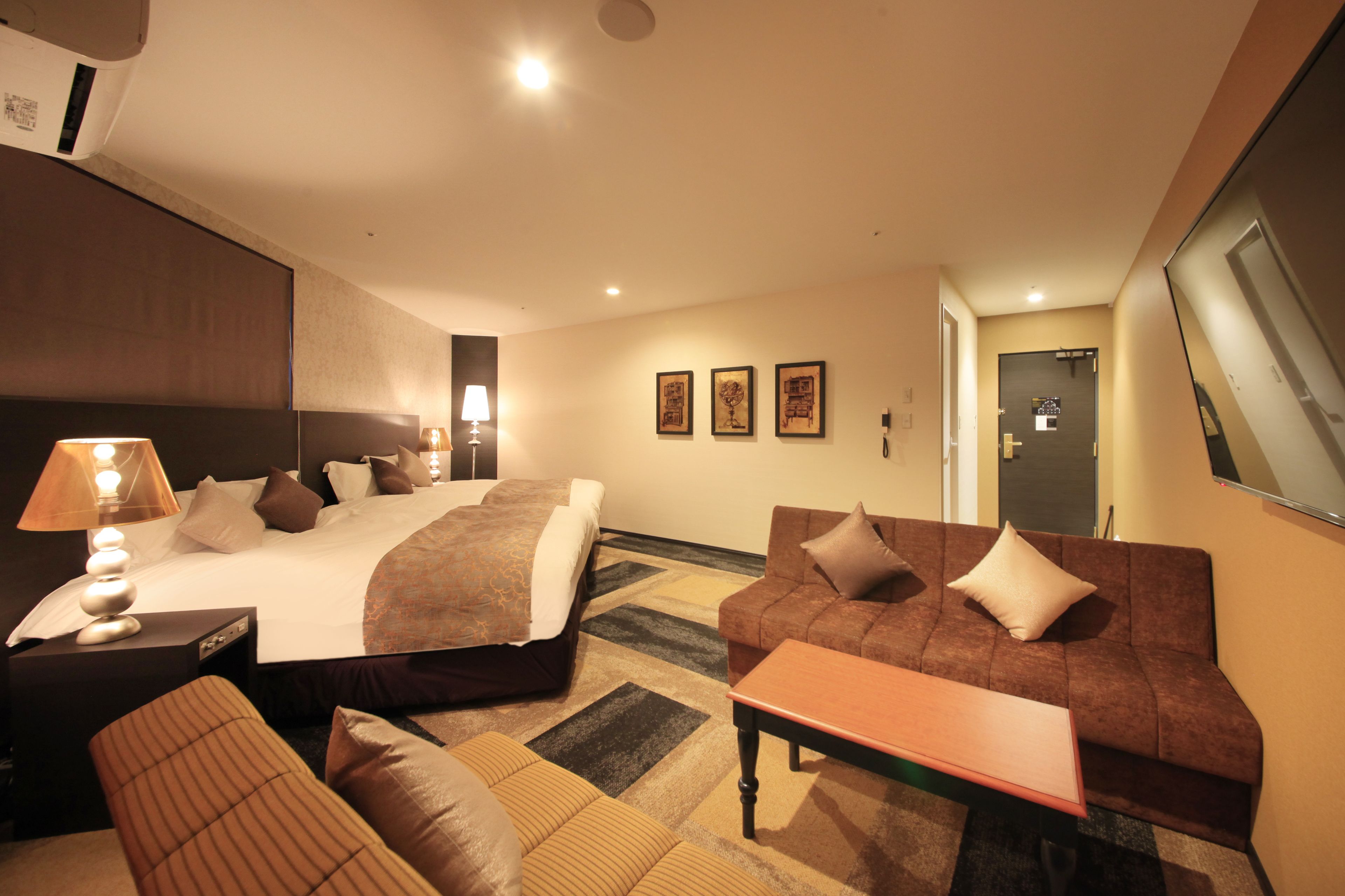 A hotel room with a large bed, a sofa, a small table, and a lamp.
