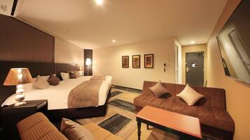 A hotel room with a large bed, a sofa, a small table, and a lamp.