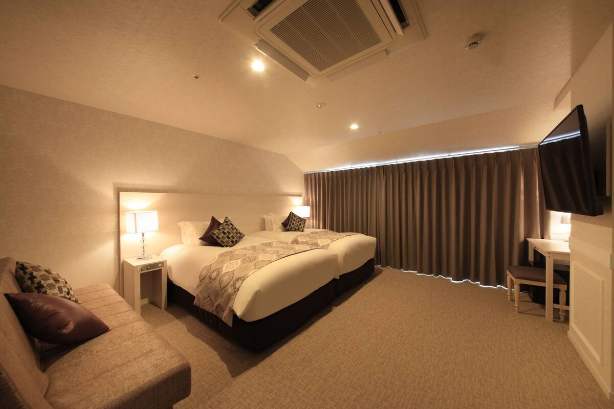 Habitación de hotel con cama, mesitas de noche, escritorio, silla y televisor.