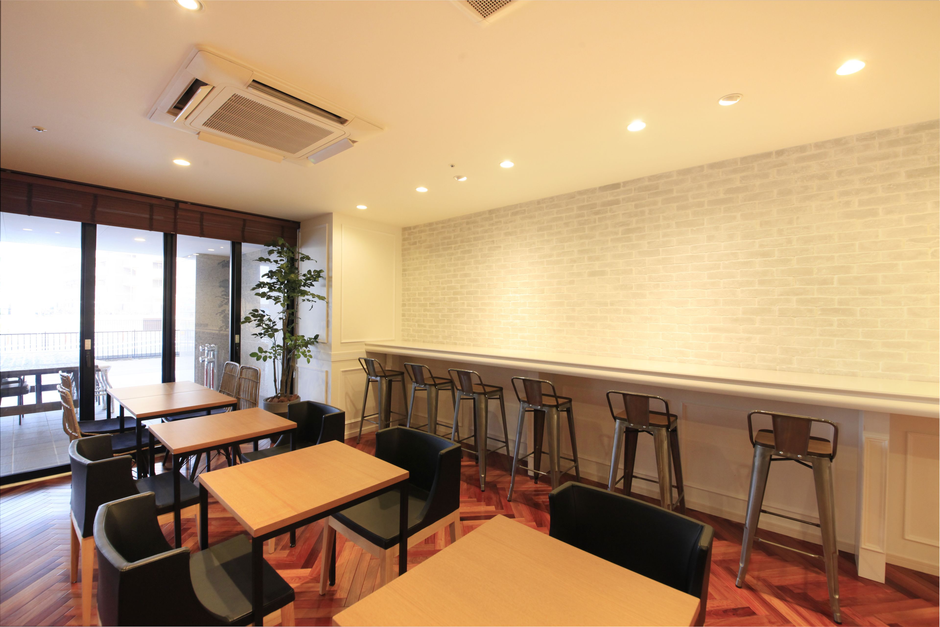 A dining area with wooden tables and chairs, a brick wall, and a potted plant.