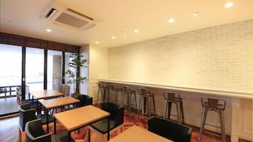 A dining area with wooden tables and chairs, a brick wall, and a potted plant.