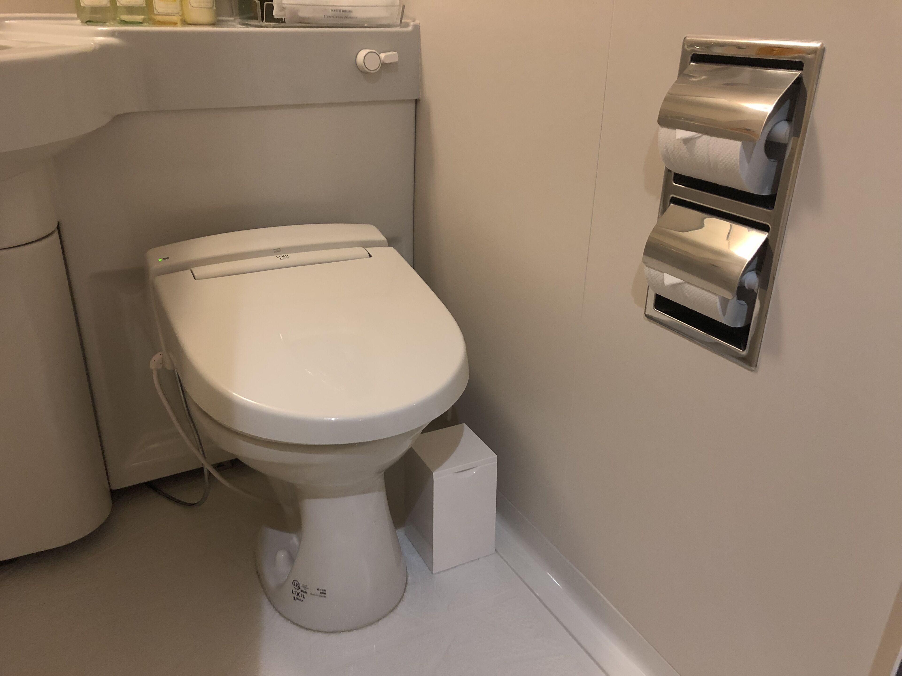 Een toilet met een bidet, een papieren handdoekdispenser en een kleine prullenbak.