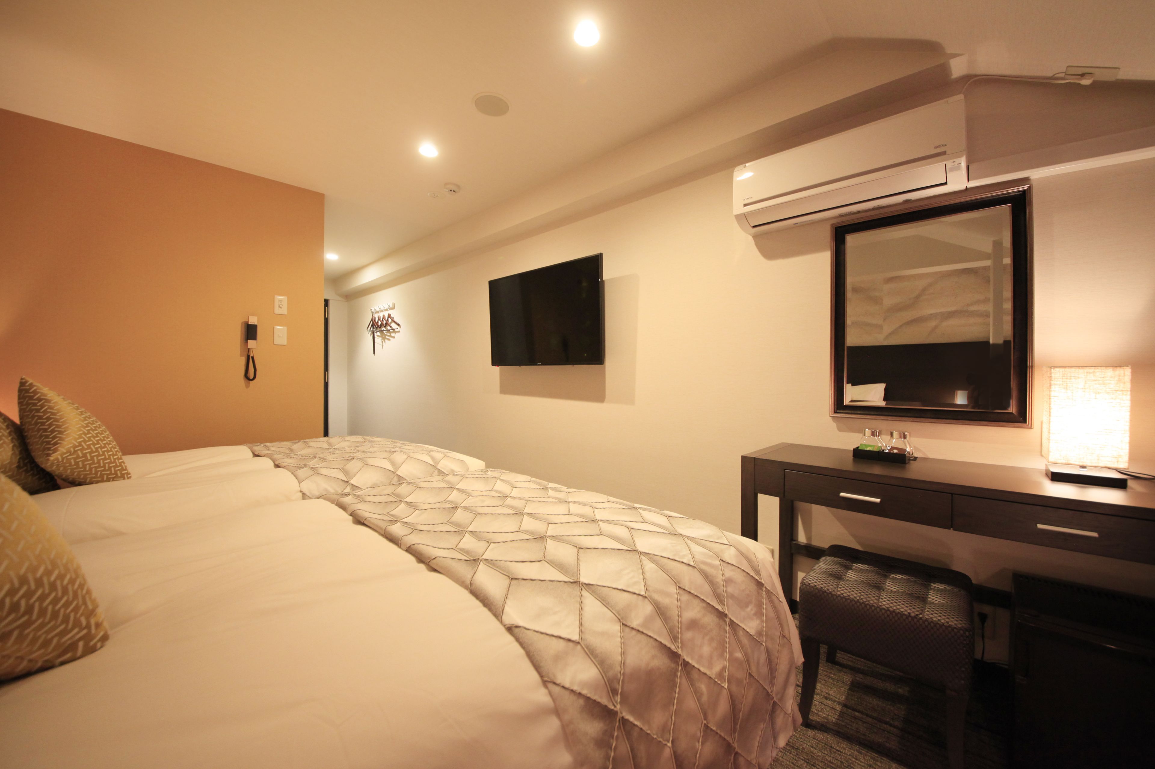 A hotel room with a large bed, a desk with a mirror, and a flat-screen TV mounted on the wall.