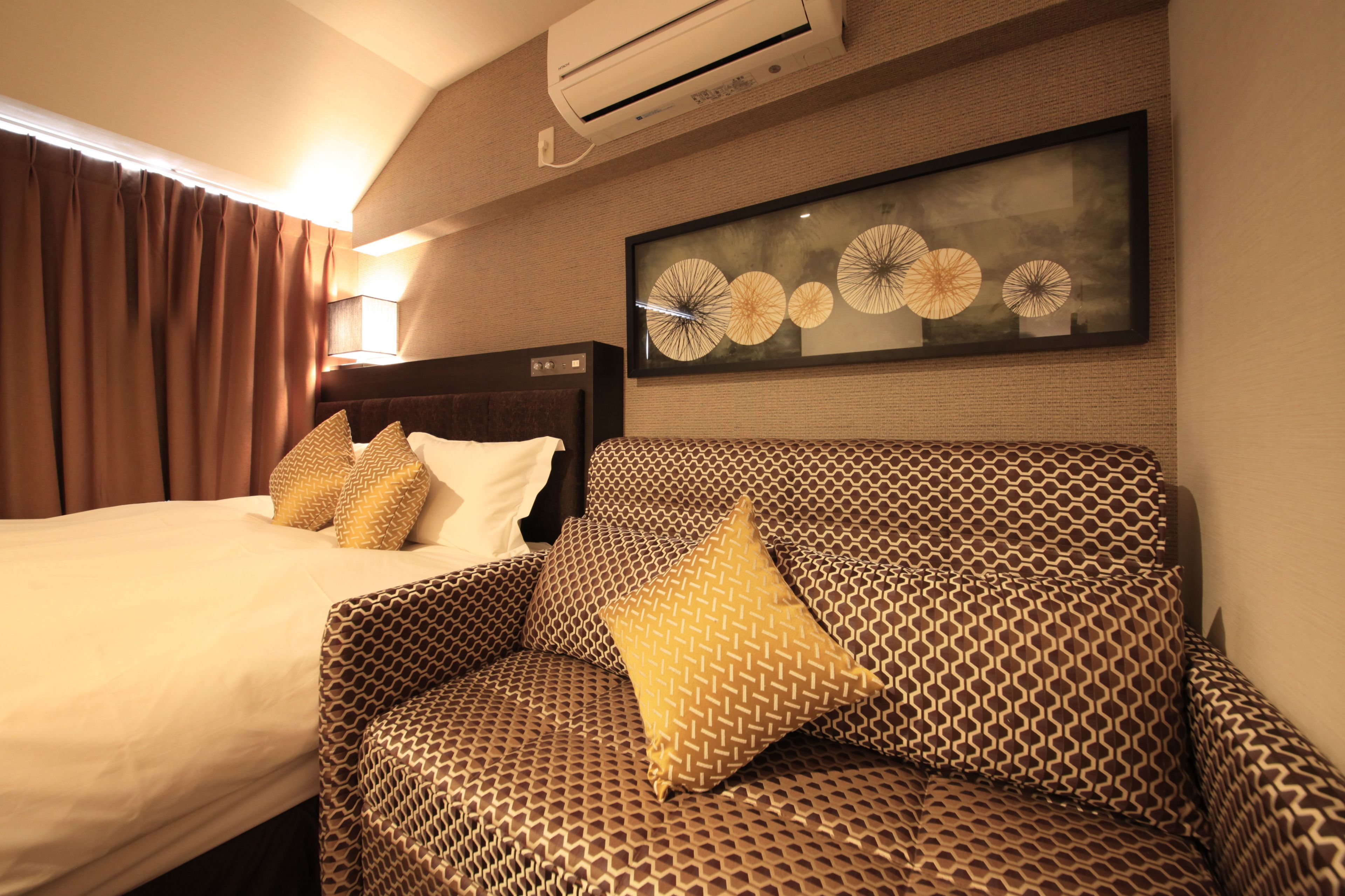 A hotel room with a bed, a sofa, and a wall-mounted air conditioner.