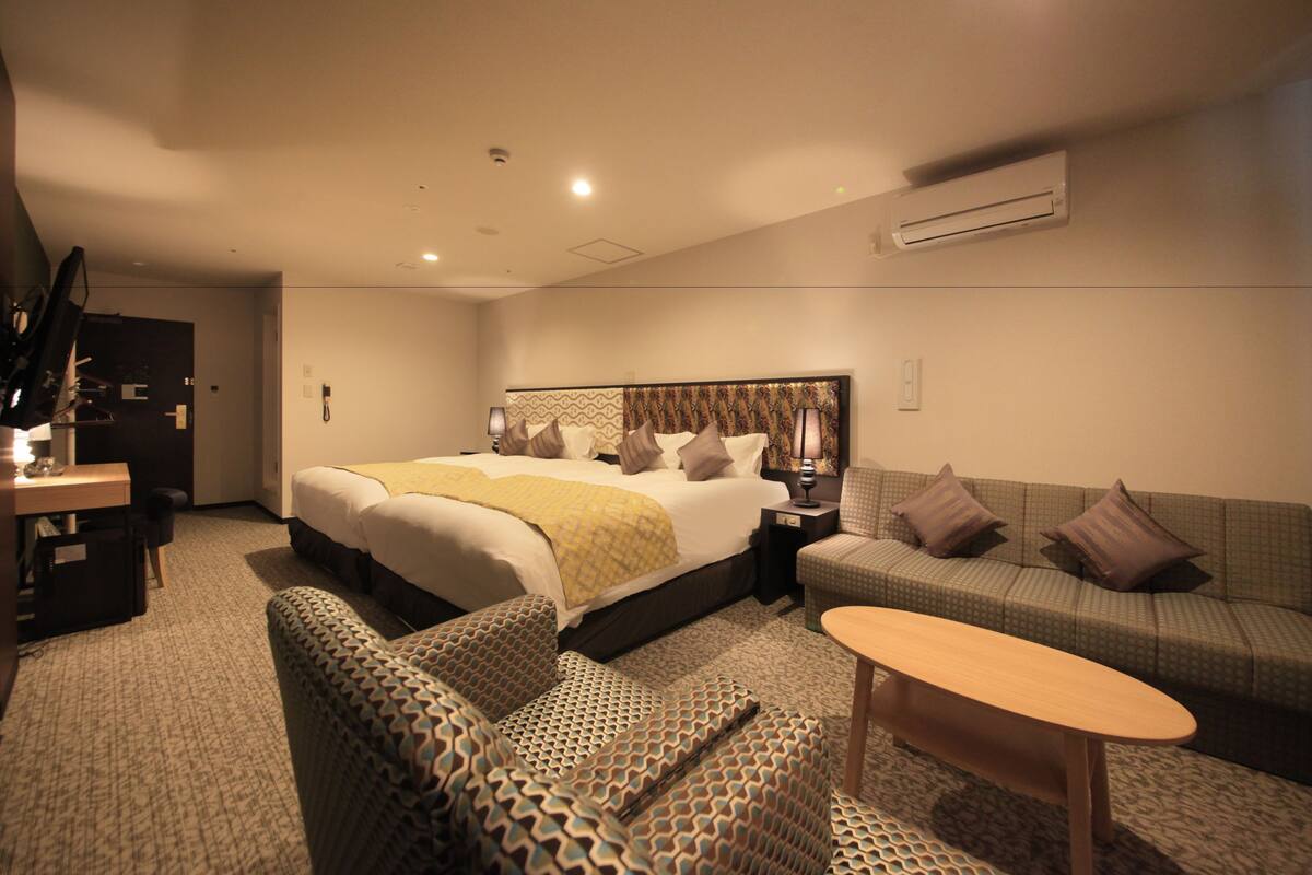 Habitación de hotel con una cama grande, un sofá, una mesita y un escritorio con lámpara.