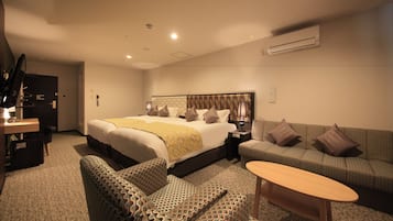 A hotel room with a large bed, a sofa, a small table, and a desk with a lamp.