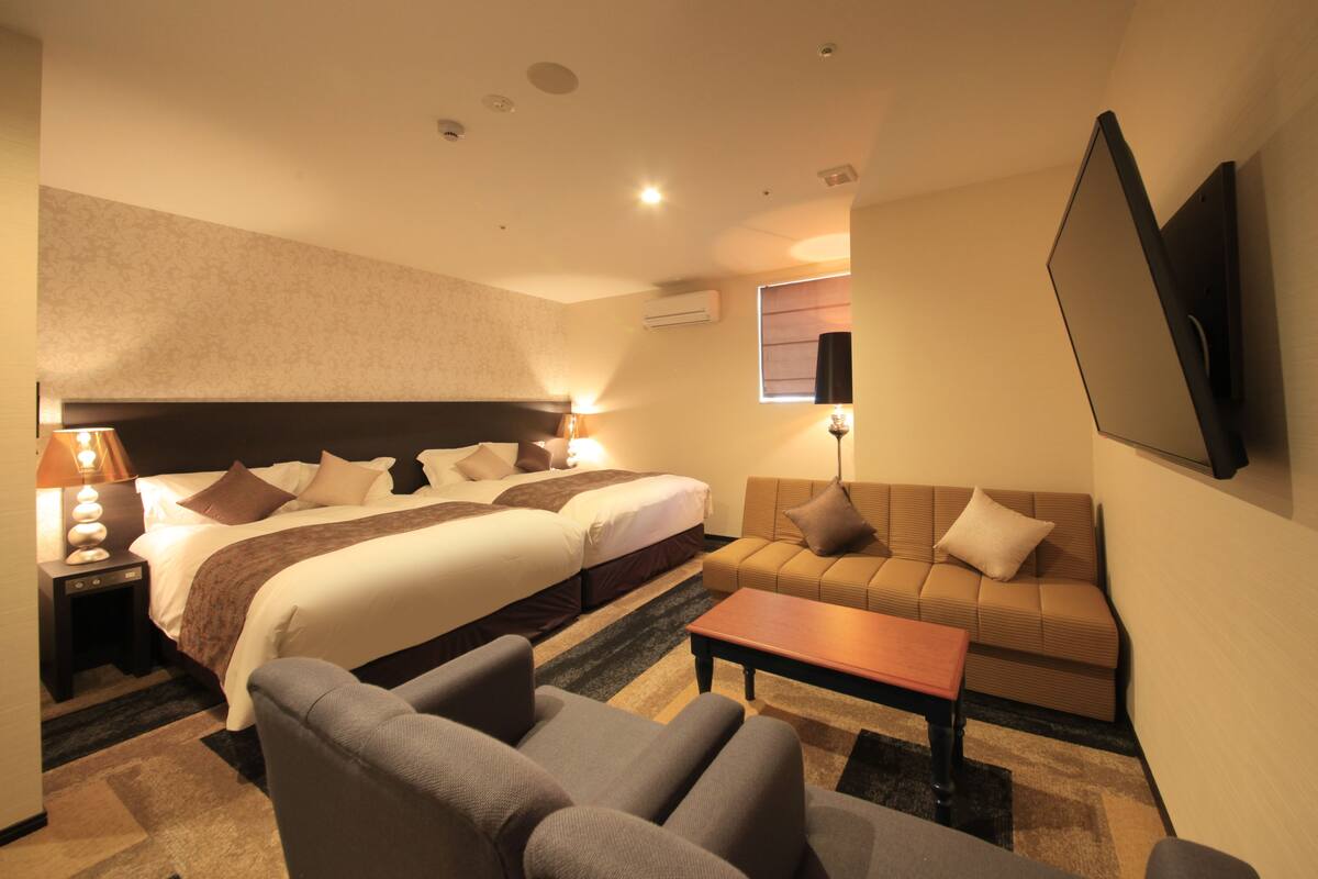 Una habitación de hotel con una cama grande, un sofá, una mesita de centro y un televisor montado en la pared.