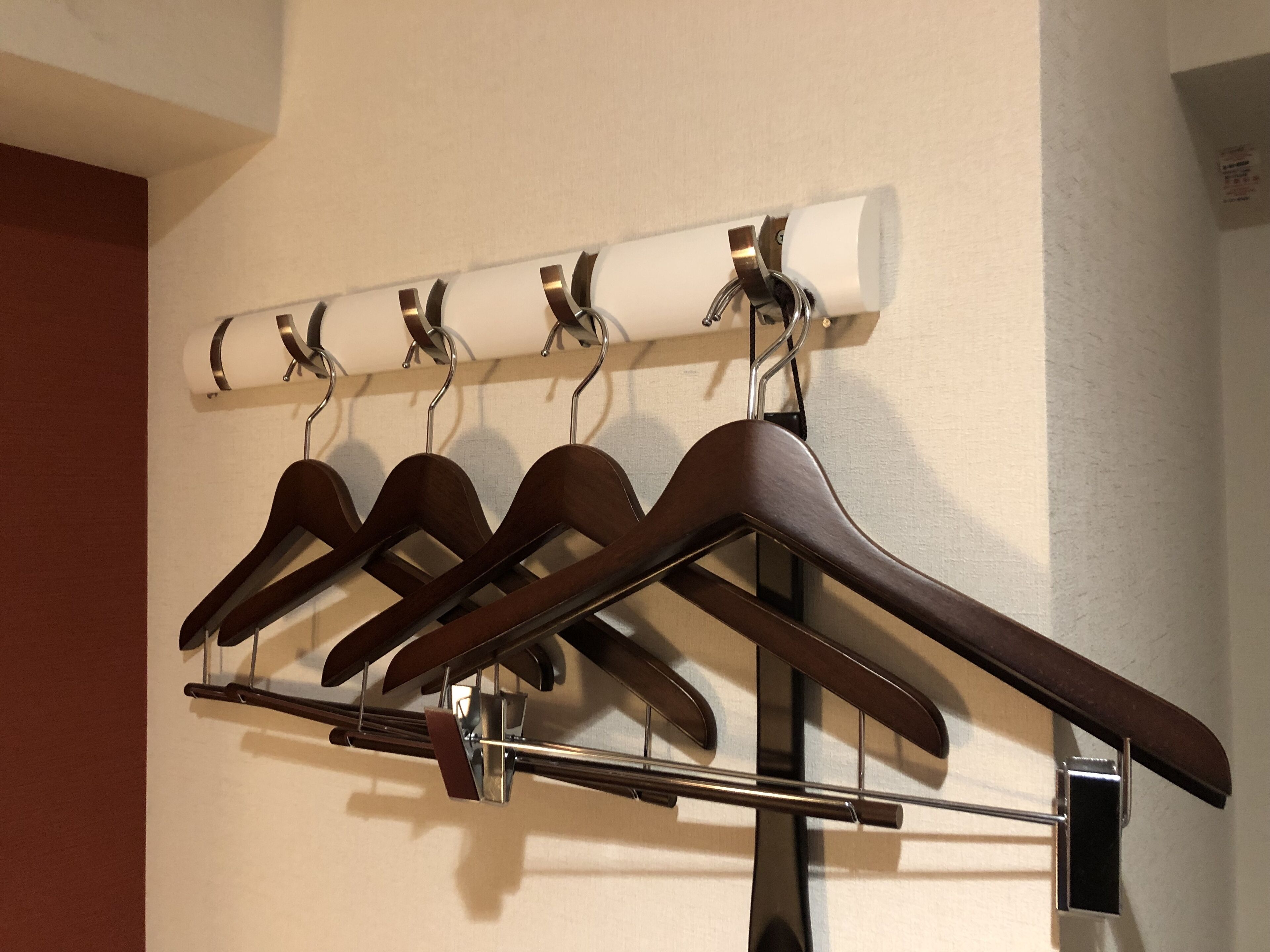 A wall-mounted coat rack with four brown hangers and a white towel dispenser.