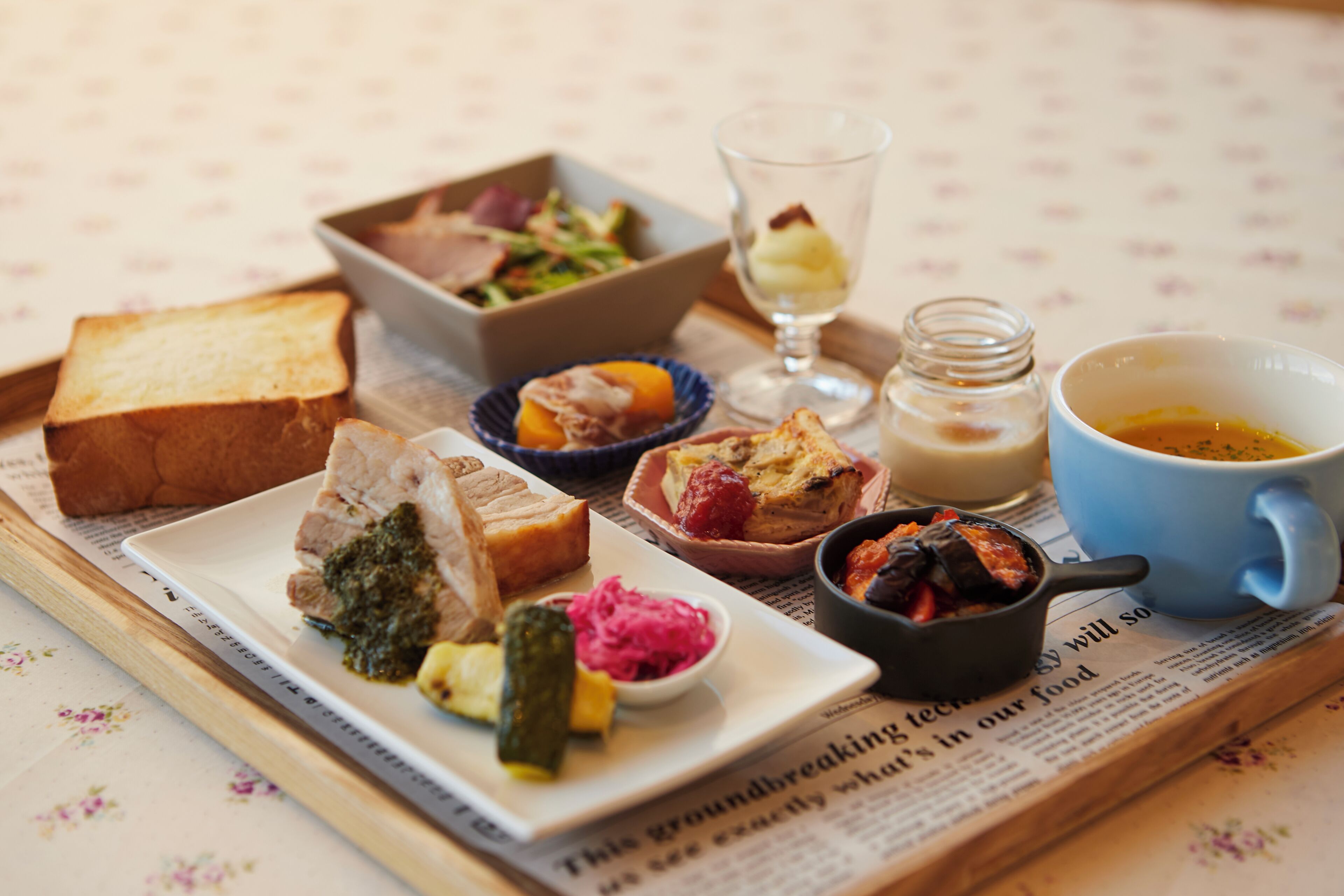 A meal with various dishes and drinks on a table with a newspaper underneath.