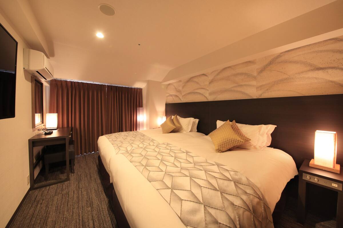 Una habitación de hotel con una cama grande, un escritorio, una mesita de noche y un aire acondicionado de pared.