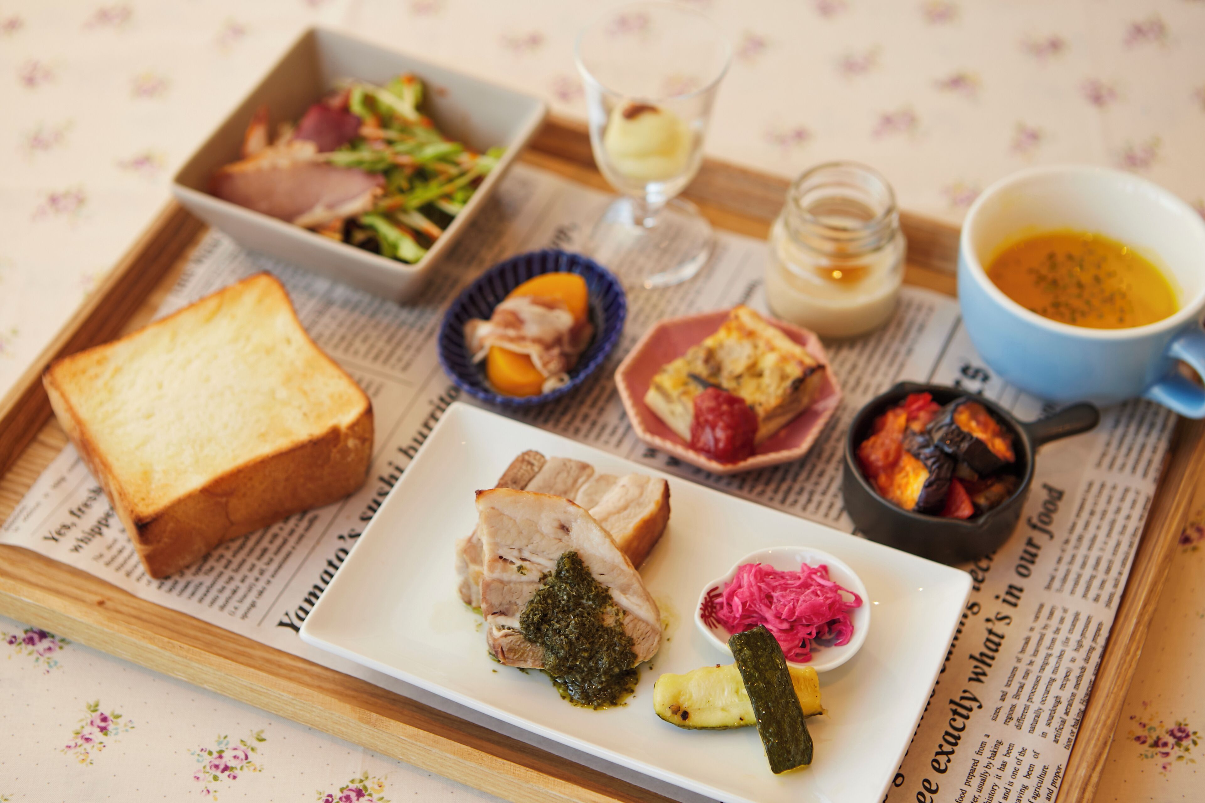 Un plateau contenant divers aliments, notamment des toasts, une salade, un plat de viande, des cornichons et une tasse de soupe.