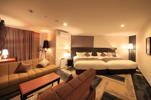 A hotel room with a large bed, a sofa, a small table, and two lamps.