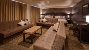 Una habitación de hotel moderna con una cama grande, dos sofás, una mesa de centro de madera y un escritorio con una lámpara.