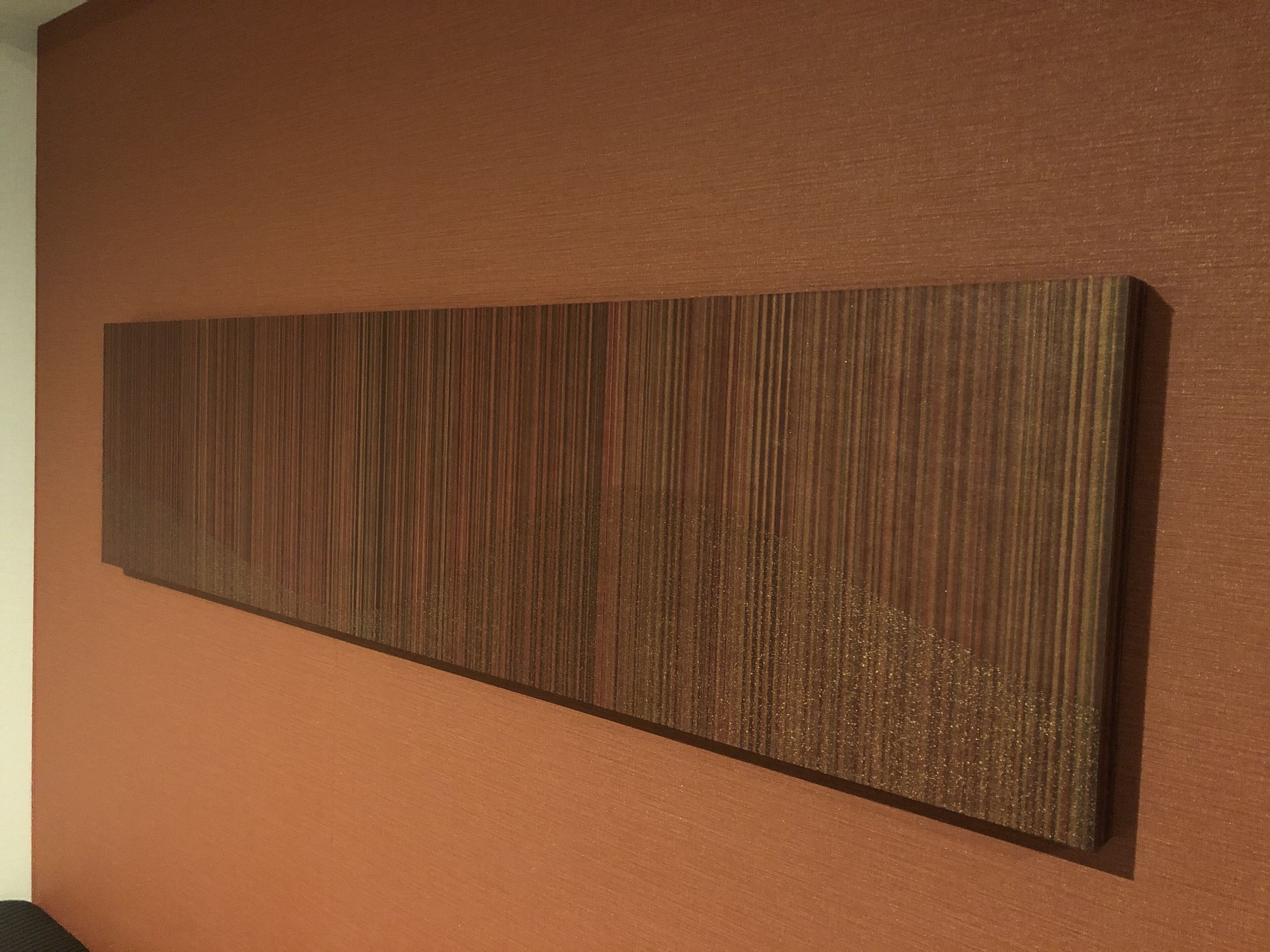 A rectangular artwork with vertical lines on a brown wall.