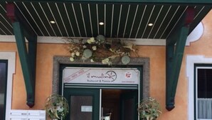 A building with a green awning, a sign reading "Il Mulino Restaurant & Pizza," and two potted plants at the entrance. - Hotel Il Mulino (Seekirchen am Wallersee)