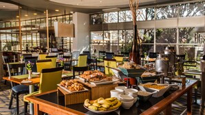 Montaje tipo bufé con diversas opciones de comida y una estación de café en un moderno comedor con ventanas amplias y luz natural.