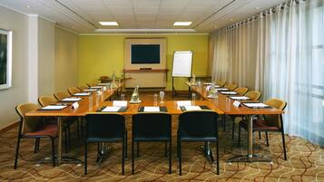 Un salón de conferencias con una mesa larga, sillas, una pantalla de proyector y una pizarra.