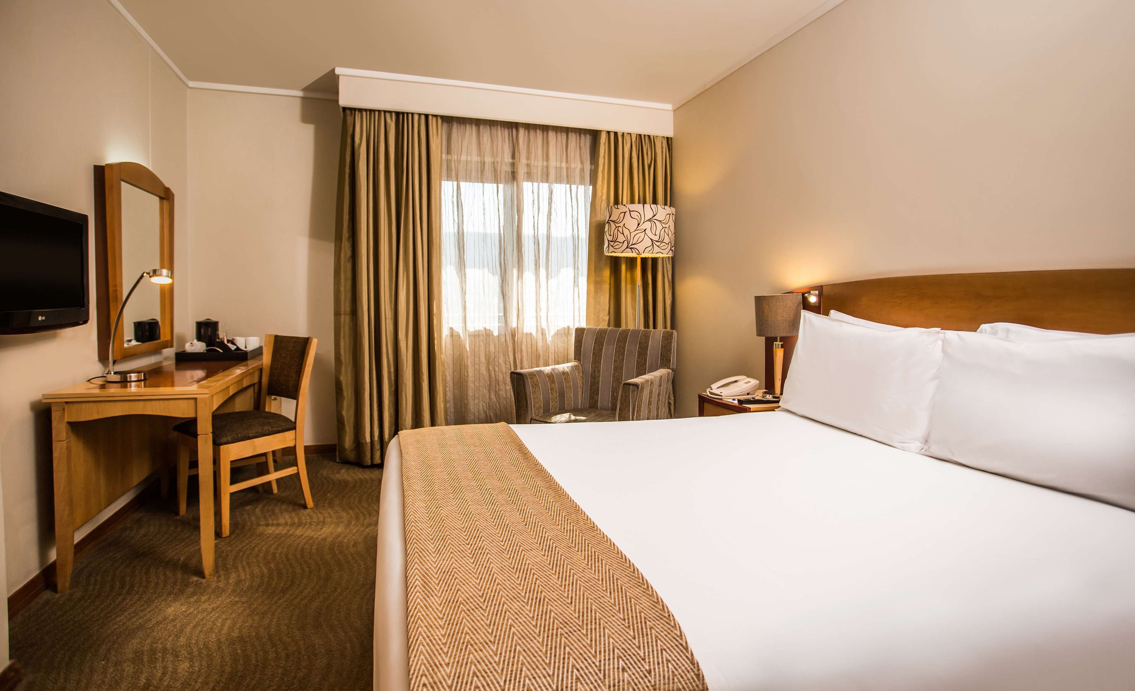 A hotel room with a bed, a desk, a chair, a television, and a window with curtains.