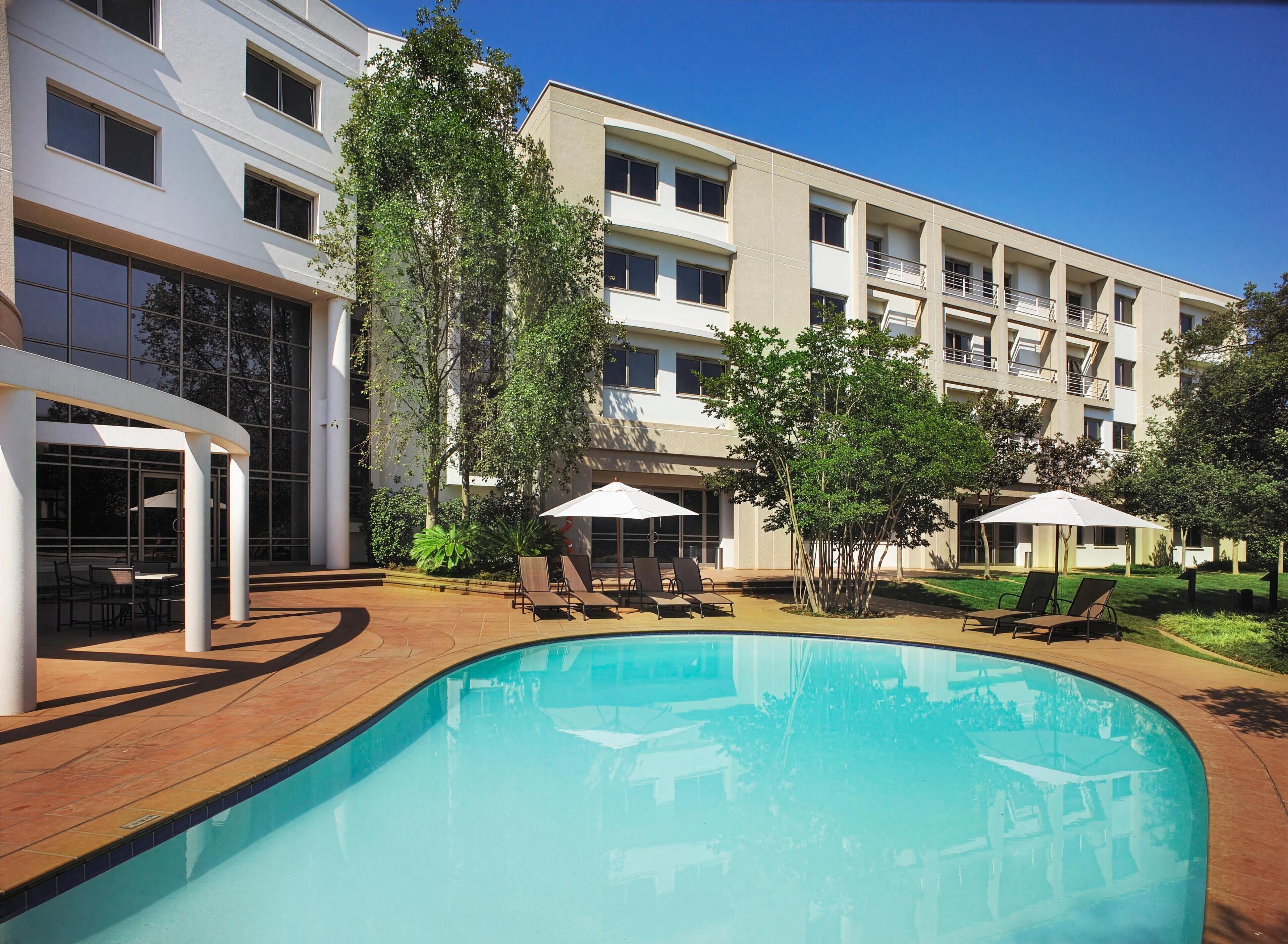 Un hotel moderno con piscina, mobiliario exterior y un jardín bien cuidado.