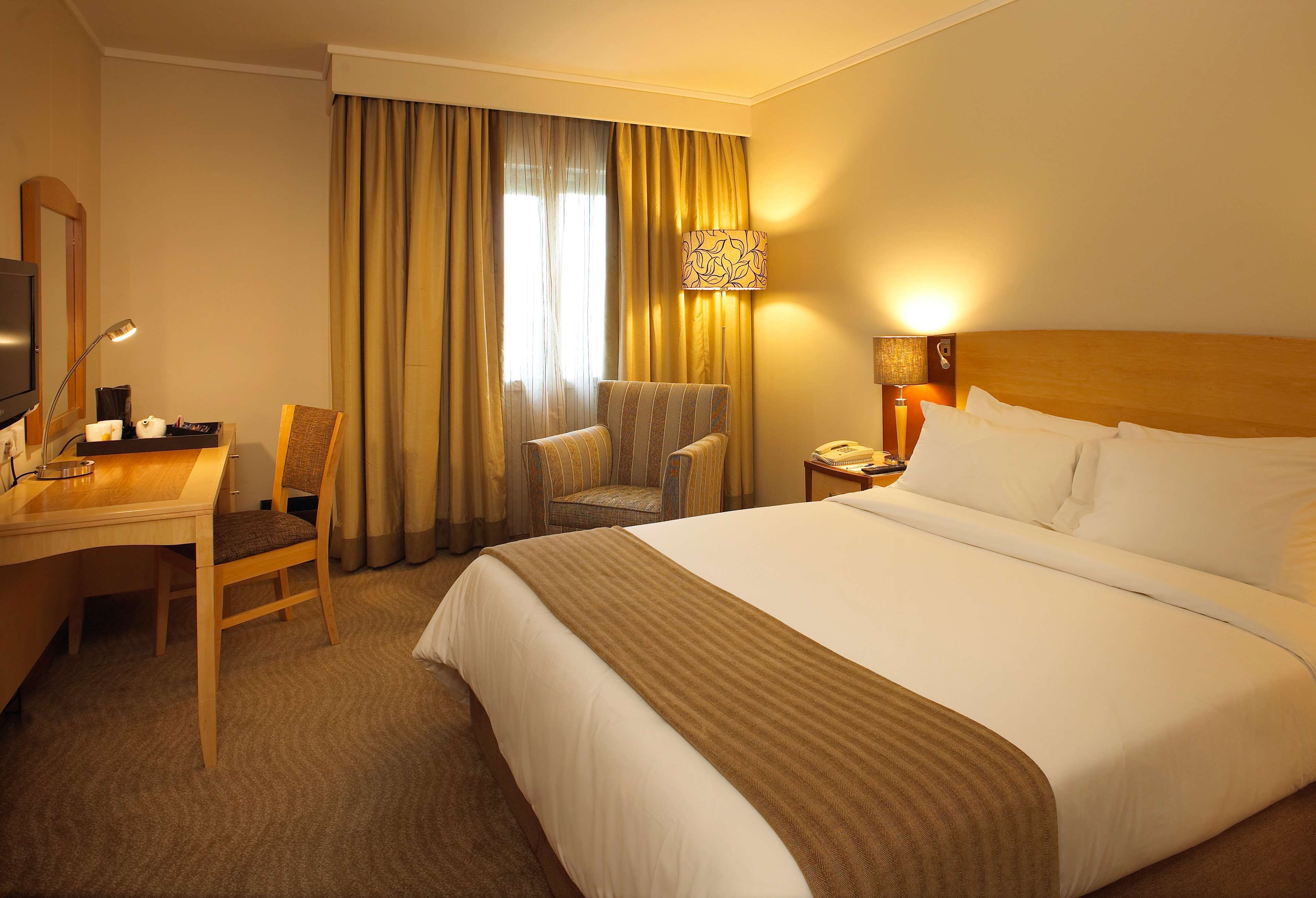 Une chambre d’hôtel avec un lit, un bureau, une chaise, une télévision et une lampe.